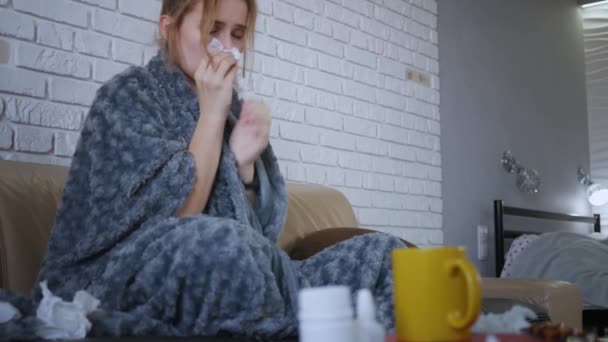 Una joven mujer caucásica sentada en un sofá con fiebre y secreción nasal usa aerosol nasal en casa. De cerca.
.  - Metraje, vídeo