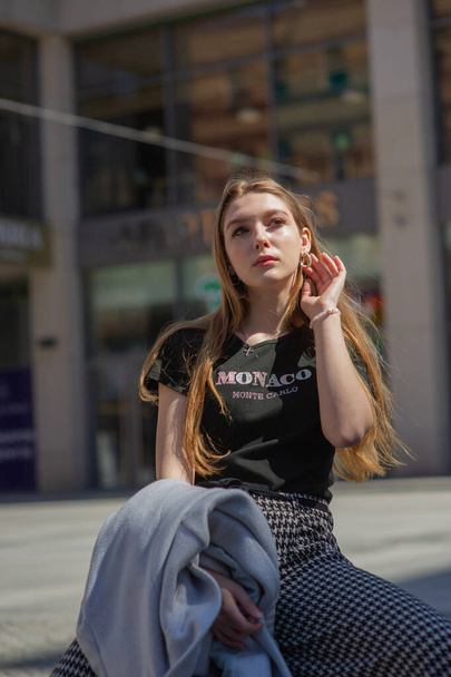 Na ulicy fotografuje się młodą dziewczynę w czarnej koszulce i szarych spodniach. Piękna kobieta na spacerze po mieście - Zdjęcie, obraz