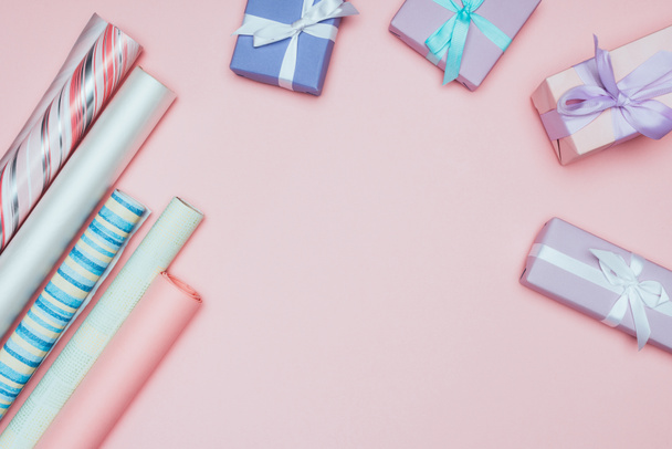 top view of christmas gift boxes with wrapping paper rolls, isolated on pink - Фото, изображение