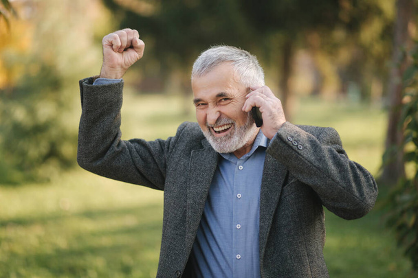 Boldog öregember beszél valakivel telefonon. Jóképű öregember, gyönyörű szakállas mosollyal és vidámsággal. - Fotó, kép