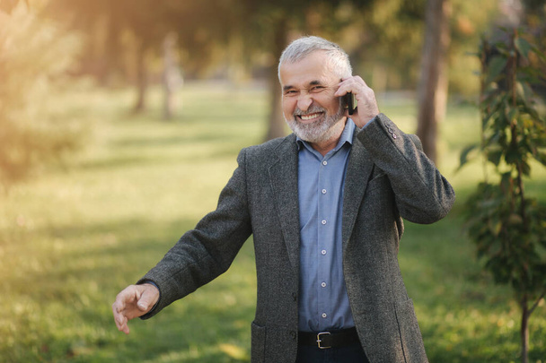 Happy elderly man speak with somebody by the phone. Handsome senior man with beautiful beard smile and rejoice - Photo, Image