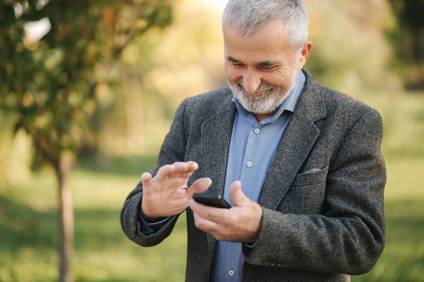 Крупним планом старий з білою бородою використовує смартфон зовні
 - Фото, зображення