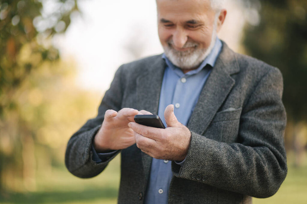 Крупный план старика с белой бородой с помощью смартфона снаружи
 - Фото, изображение