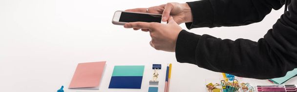 cropped view of commercial photographer making photos of flat lay with office supplies on smartphone, panoramic shot - Photo, Image