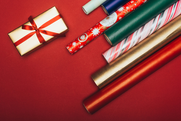 top view of wrapping paper rolls and christmas present on red - 写真・画像