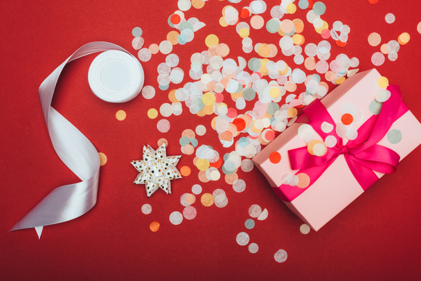 top view of one christmas present with bow, ribbon and confetti on red - Foto, Imagen