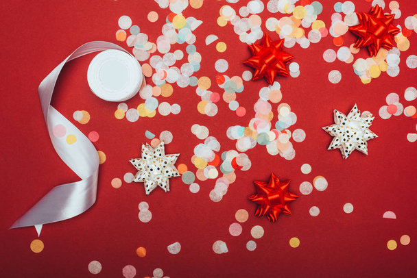 top view of christmas confetti, white ribbon and bows on red - 写真・画像