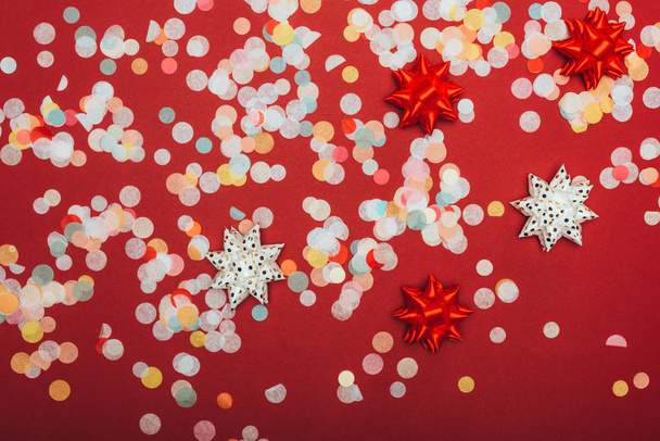 bovenaanzicht van kerst confetti en strikken op rood - Foto, afbeelding