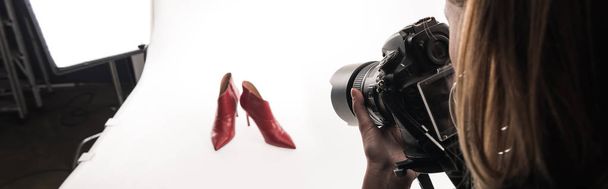 vue recadrée du photographe faisant une séance photo commerciale de chaussures à talons rouges féminines sur blanc, plan panoramique
 - Photo, image