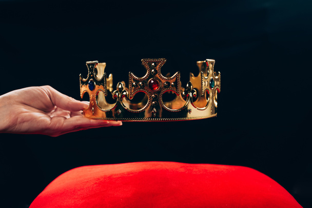 vue recadrée de la femme tenant couronne dorée avec pierres précieuses sur oreiller rouge, isolé sur noir
 - Photo, image