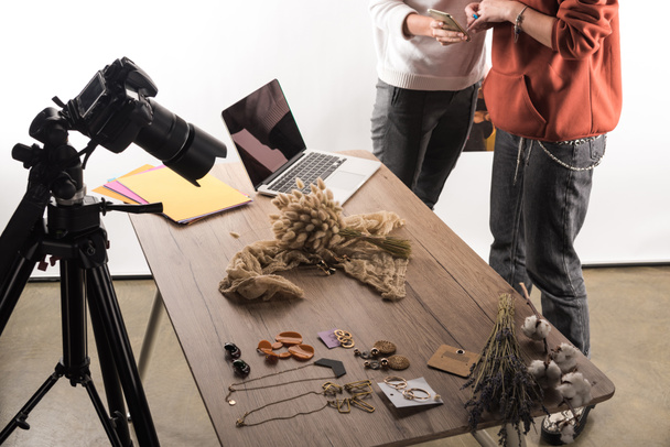 cropped view of two commercial photographers working with accessories, digital camera, laptop and smartphone - Foto, Bild