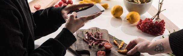 Ausgeschnittene Ansicht von zwei professionellen Fotografen, die Nahrungsmittelkompositionen für kommerzielle Fotografie auf einem Smartphone auf einem Holztisch machen - Foto, Bild