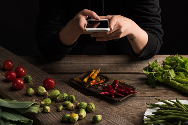 καλλιεργημένη άποψη του επαγγελματία φωτογράφου που κάνει σύνθεση τροφίμων για την εμπορική φωτογραφία στο smartphone σε ξύλινο τραπέζι - Φωτογραφία, εικόνα