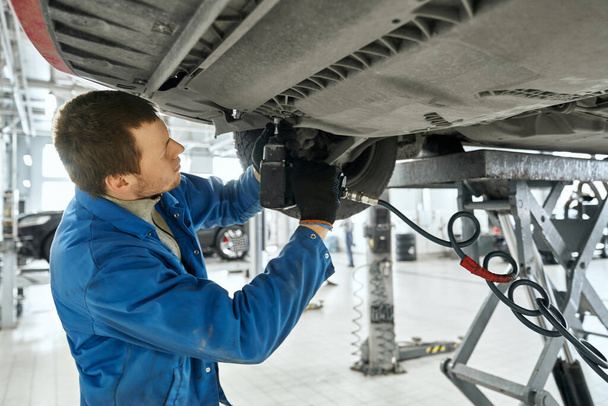 Male specialist repairing the equipment under car in garage - Fotoğraf, Görsel