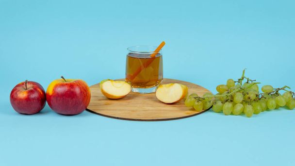 Egy pohár gyümölcslé friss szőlővel és almával kék alapon. - Fotó, kép