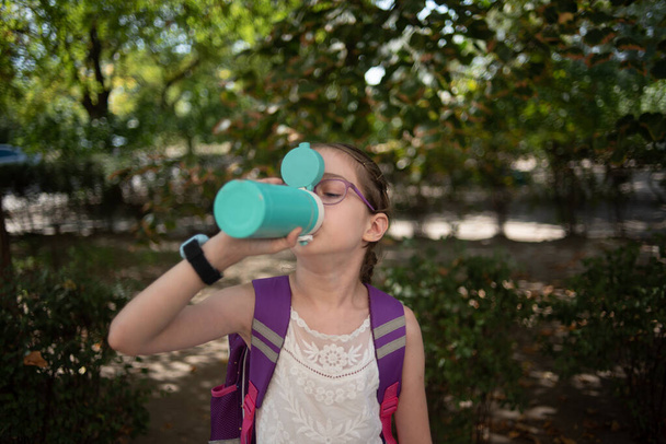 Kupás lány. Egy szemüveges iskoláslány termoszból vagy hőből iszik vizet. - Fotó, kép