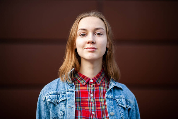 Emotions. Light smile. Teenager. Young pretty white caucasian girl in casual  jean jacket opposite dark modern backgroun on the street in the autumn. - Foto, Imagem