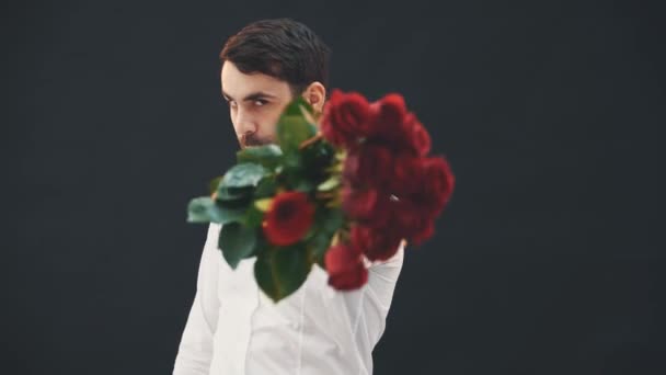 Funny young man fencing by a bouquet of red roses as if it was sword. Then smells it, puts it on the shoulder, going away. - Footage, Video