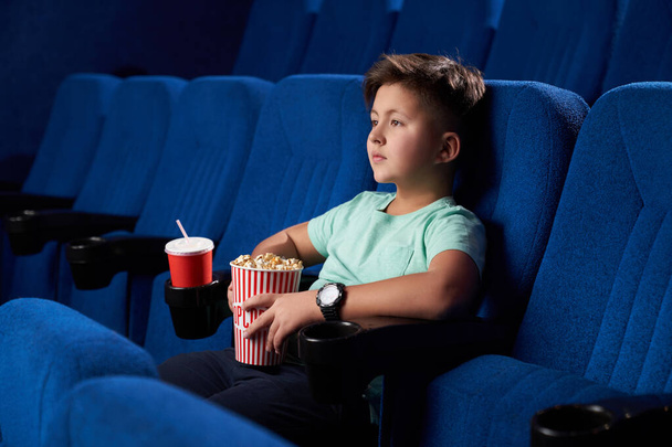 Side view of relaxed male teen eating junk food in cinema - Фото, изображение