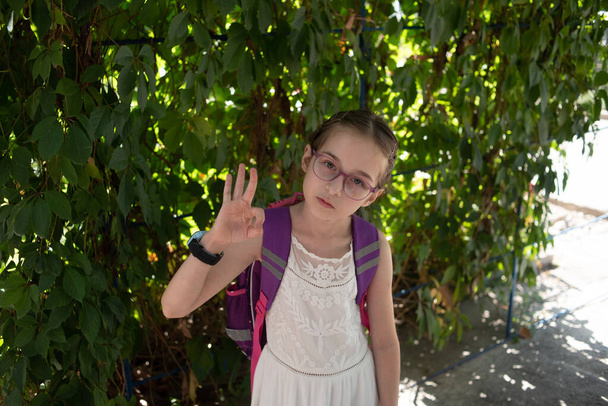 Uczennica w fioletowym plecaku i fioletowych okularach. Dziewczyna w białej sukience, nosi okulary jesienią. - Zdjęcie, obraz