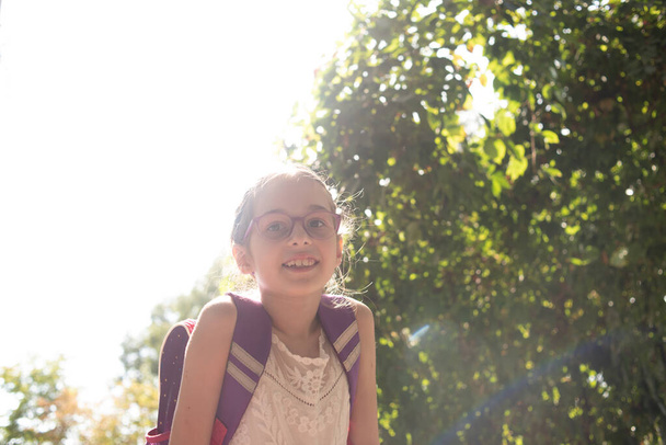 Écolière avec un sac à dos violet et des lunettes violettes. Fille en robe blanche, portant des lunettes en automne
. - Photo, image