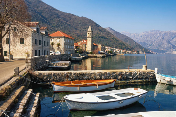 Piccolo villaggio mediterraneo contro le montagne. Montenegro, Mare Adriatico. Veduta della baia di Kotor e del villaggio di Stoliv nella soleggiata giornata invernale
 - Foto, immagini