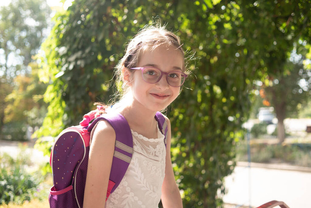 Écolière avec un sac à dos violet et des lunettes violettes. Fille en robe blanche, portant des lunettes en automne
. - Photo, image