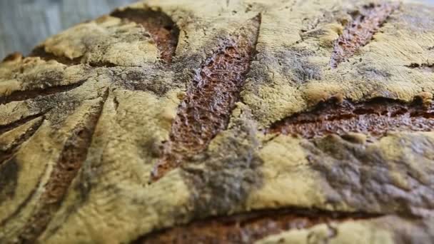 makro zaměření z celé velké domácí kulaté černý žitný chléb se zajímavou povrchovou texturou na tmavém dřevěném stole - Záběry, video
