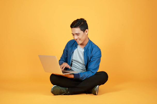 Азиатский человек использование ноутбука на цветном оранжевом фоне
 - Фото, изображение