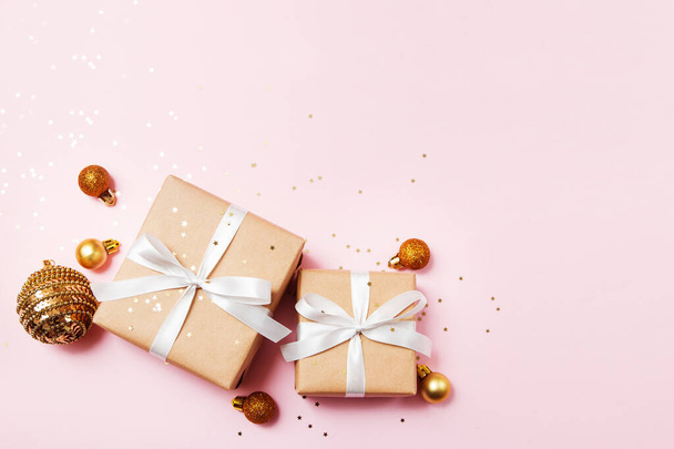 Weihnachtsgrußkarte Komposition. Bastelpapier-Geschenke mit weißem Band auf rosa Hintergrund mit goldenen Weihnachtskugeln und Konfetti-Stern. flache Lage, Draufsicht, trendiger Stil. - Foto, Bild