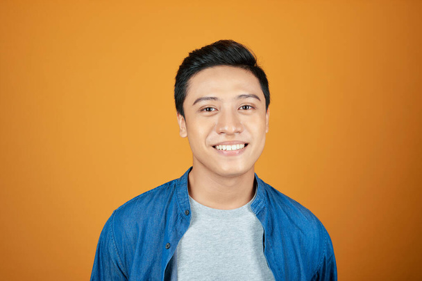 Portret van jonge Aziatische man glimlachend geïsoleerd op oranje achtergrond - Foto, afbeelding