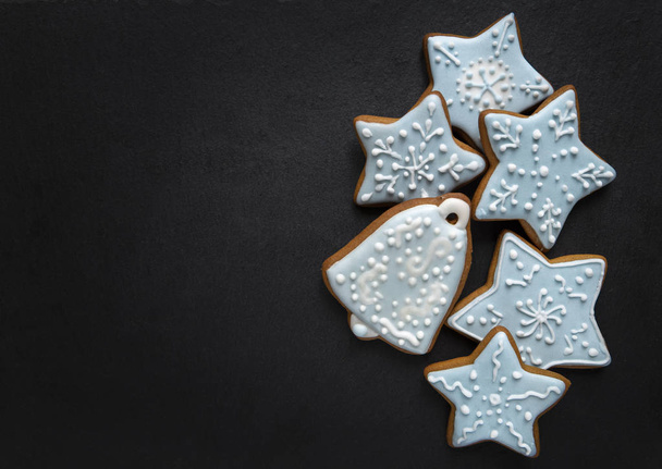 Homemade gingersnaps covered with icing on the dark plate: bell and stars; delicious cookies with Christmas shapes - Foto, Imagen