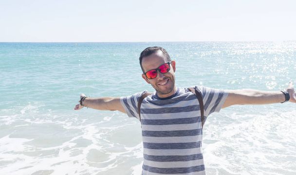 Nuoren parrakkaan miehen muotokuva seisomassa rannalla aurinkoisena päivänä.
 - Valokuva, kuva