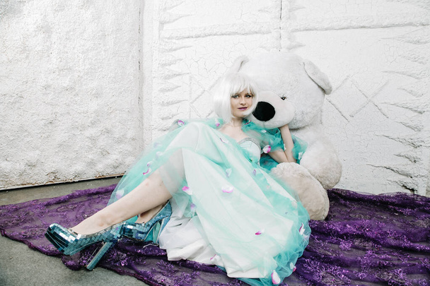 mooi blond volwassen meisje in schattig blauw jurk met grote wit teddy beer - Foto, afbeelding