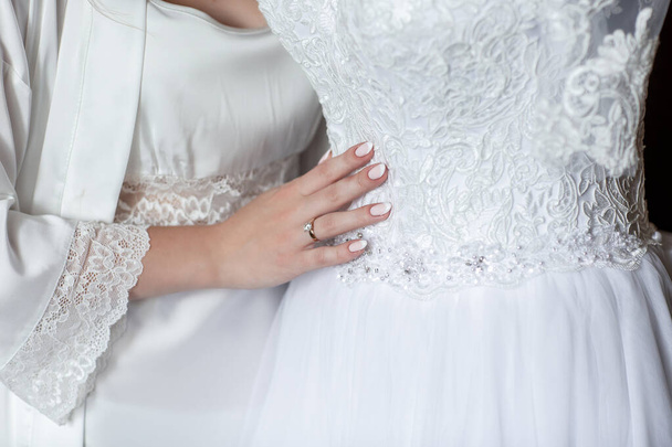 Tolles Kleid. schöne junge Frau im seidenen Bademantel, die ihr Hochzeitskleid berührt. Detail eines eleganten weißen Hochzeitskleides - Foto, Bild