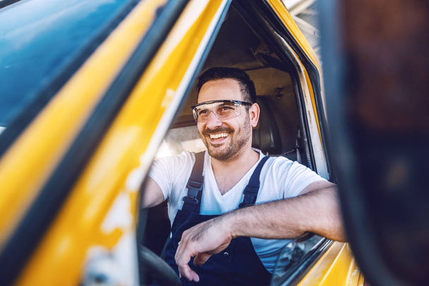 Smiling handsome unshaven worker driving vehicle on construction site. - 写真・画像