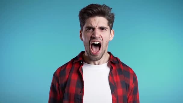 Young european stressed man in red shirt shouting isolated over blue background. Slow motion. Stressed and depressed guy loudly screaming to camera. - Metraje, vídeo