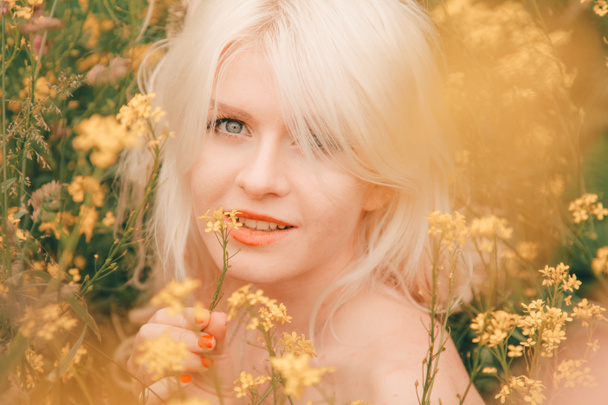 beautiful young blonde woman on the meadow with yellow flowers on a warm summer day - Photo, Image