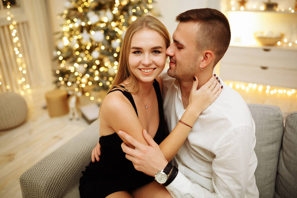 couple in love kisses and hugs on the sofa near the Christmas tree lights. New year's night. Christmas. - Foto, Imagen