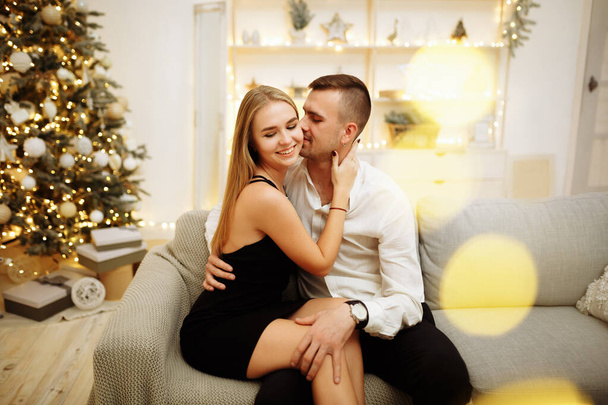 пара закоханих поцілунків і обіймів на дивані біля ялинкових вогнів. Новорічна ніч. Різдво
. - Фото, зображення