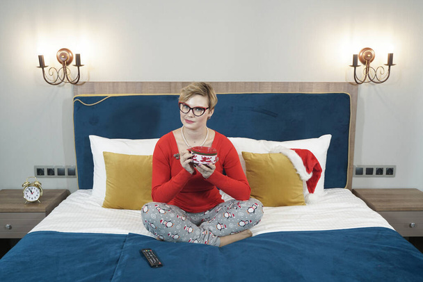 Güzel bir kadın, elinde bir fincan kahveyle yatak odasında oturuyor. - Fotoğraf, Görsel