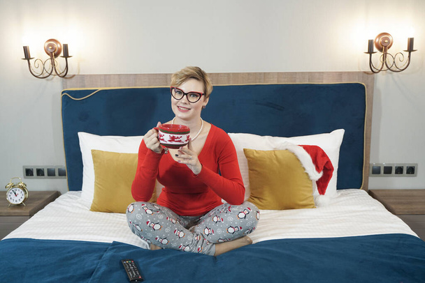 Piękna kobieta z filiżanką kawy siedzi na łóżku w sypialni - Zdjęcie, obraz
