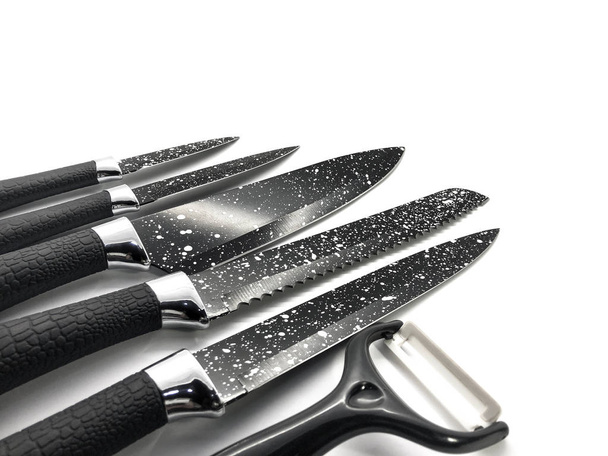 Set of professional black knives and peeler isolated on a white background. Composition of the chef knife, bread knife, utility knife, paring knife and ceramic peeler. - Photo, Image