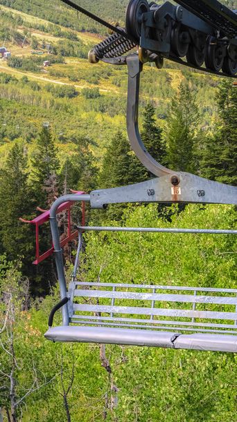 Κάθετη Κοντινό πλάνο ενός ανελκυστήρα καρέκλα πάνω από το βουνό με μονοπάτια πεζοπορίας και δέντρα εκτός εποχής - Φωτογραφία, εικόνα