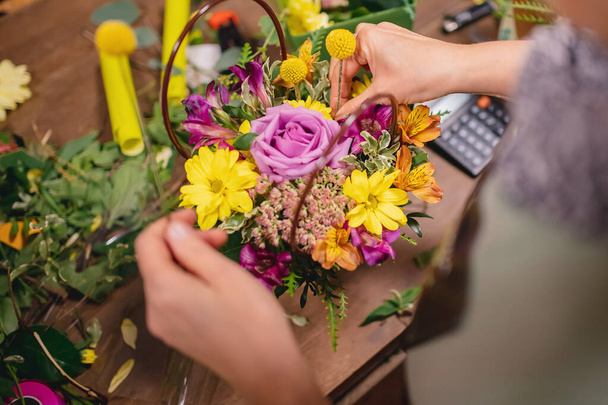 Florist woman makes bouquet flowers of pink roses, yellow chrysanthemums in gift box. Top view on workplace. Concept considers value business calculator - Photo, Image