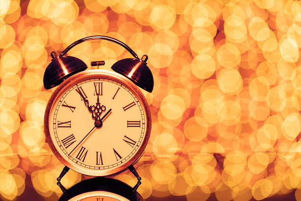Nochevieja medianoche. Reloj despertador retro cuyo puntero muestra de cinco a doce en el fondo festivo bokeh
 - Foto, imagen
