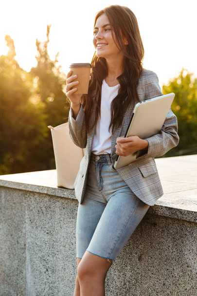 Щаслива молода бізнес-леді тримає ноутбук комп'ютер п'є каву
. - Фото, зображення