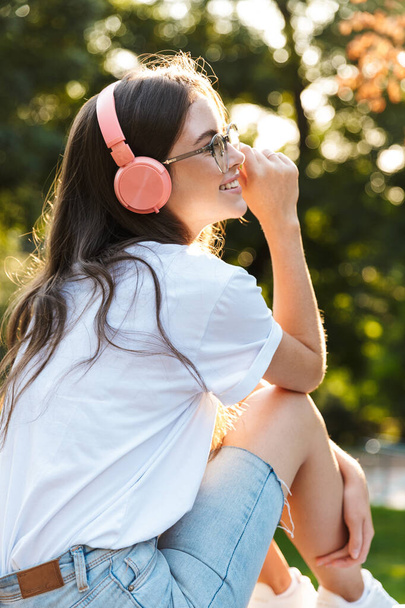 Lady outdoors in nature green park listening music with headphones. - Foto, Imagen