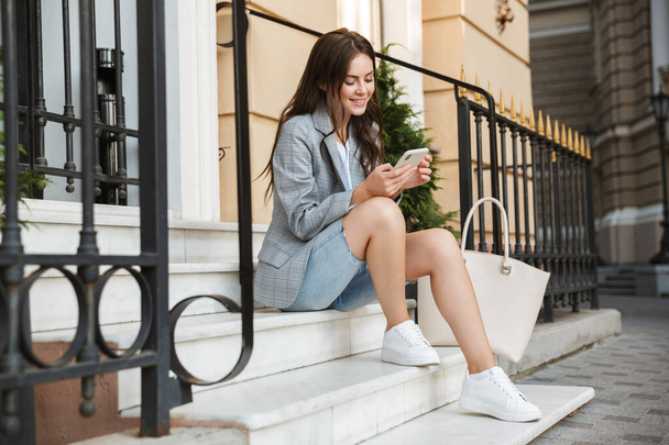 Business lady outdoors at the street using mobile phone sit on steps. - Foto, imagen