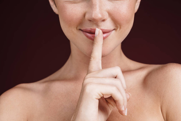 Cropped image of happy shirtless woman holding finger at her lip - Photo, Image